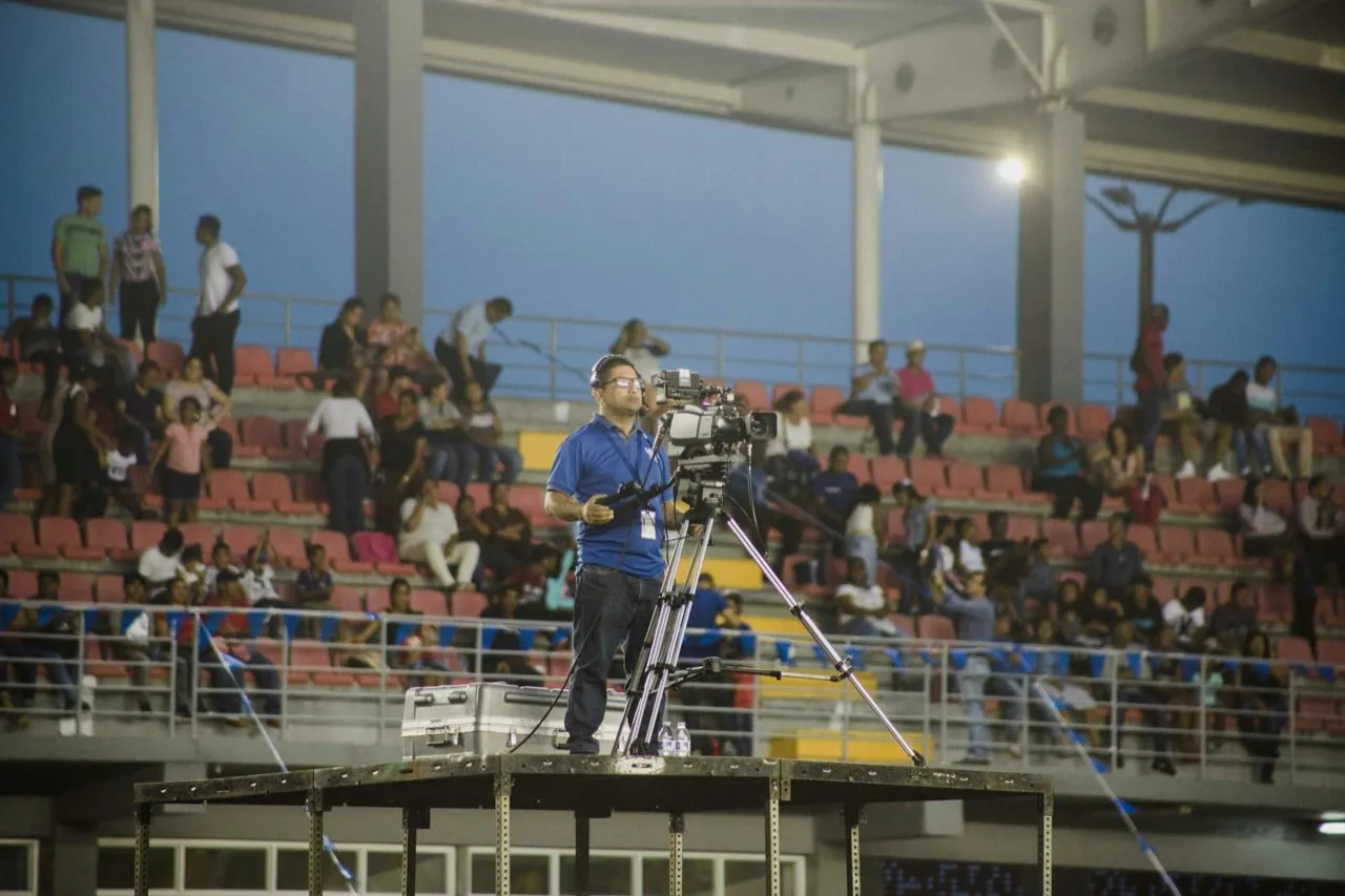A camera operator filming a match from a raised platform above a stadium crowd