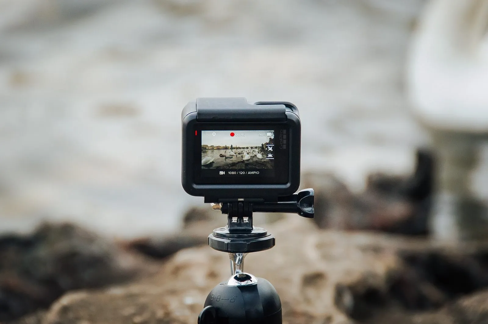 A small action camera on a mini tripod, its rear screen showing the shot it is recording