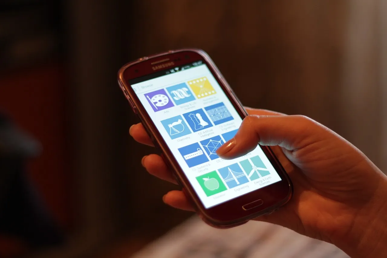 A hand holding a Samsung Android phone with a grid of app icons on the screen