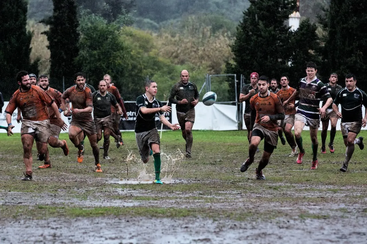Amateur players chasing the ball across a muddy pitch in heavy rain