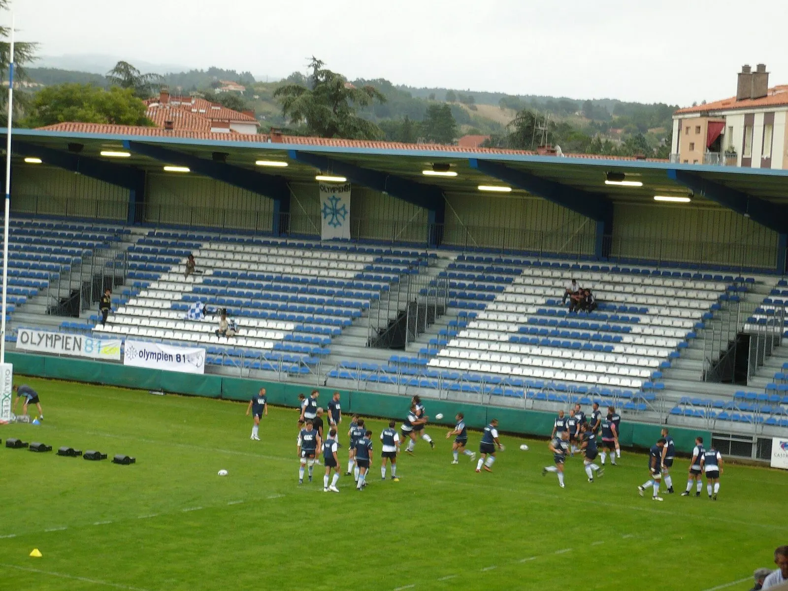 A professional rugby squad in training vests warms up in front of an almost empty stand before a match