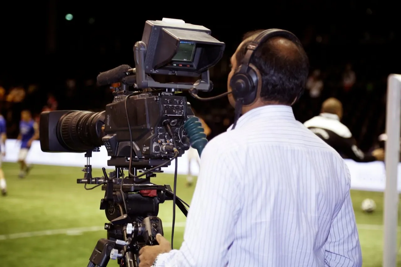 A camera operator filming a match pitchside with a broadcast camera