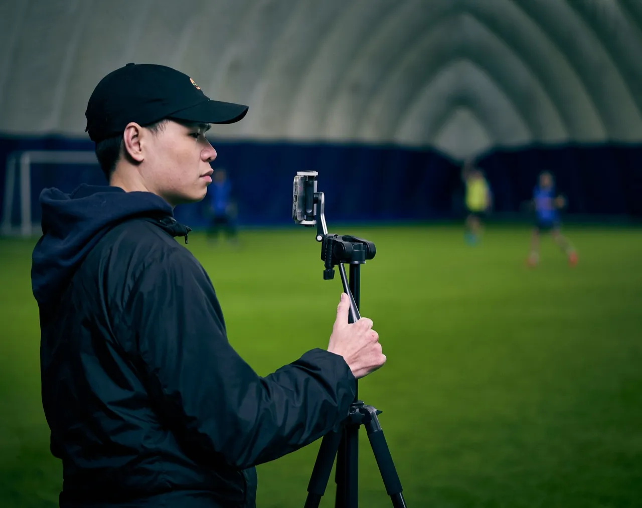 A person filming a training session on a phone tripod inside an indoor dome pitch
