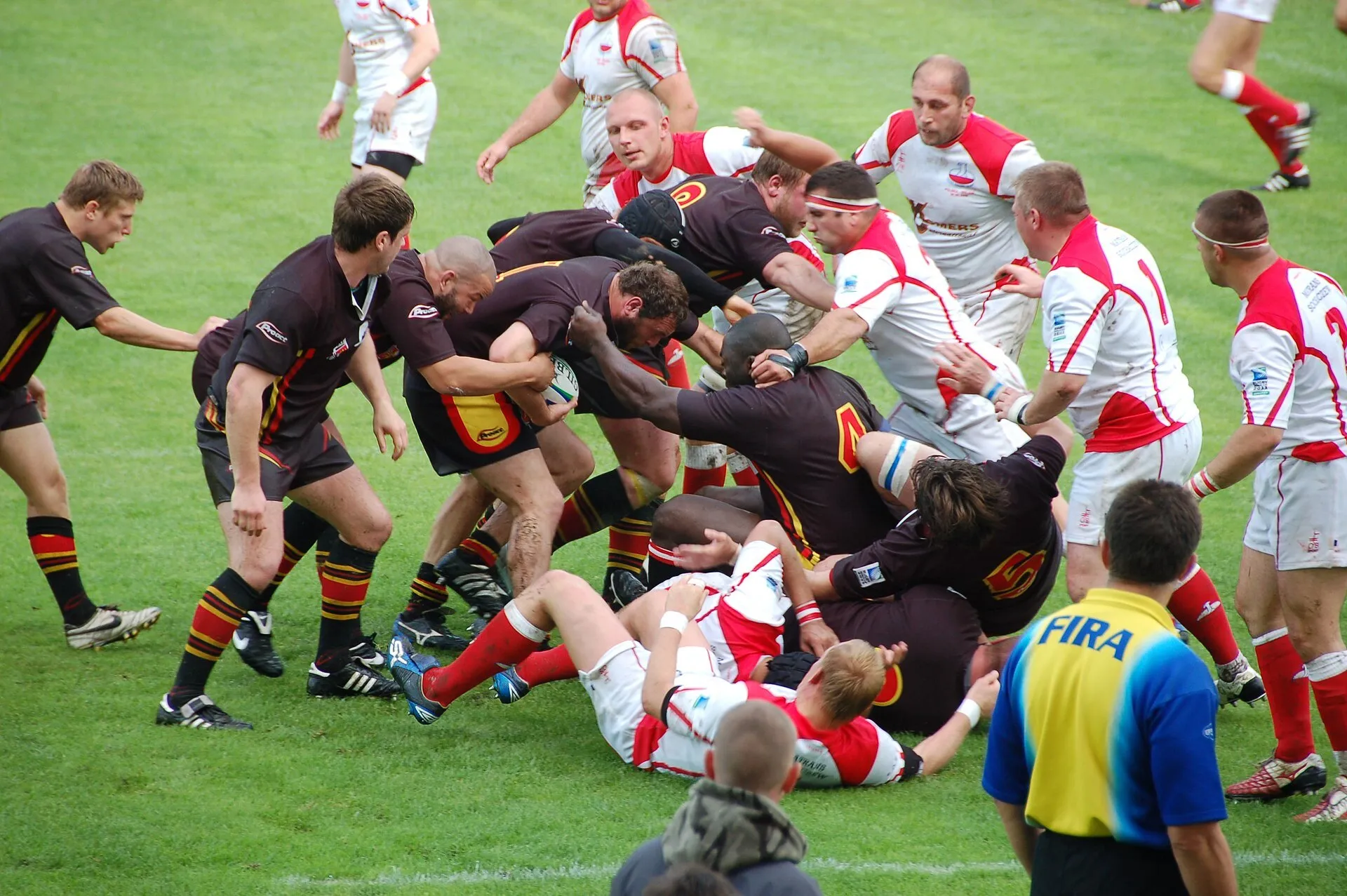 Players from both sides pile into a ruck during a match, with the referee watching from close range