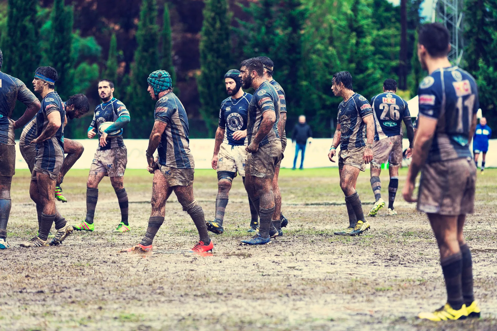 A rugby team caked in mud walking back into position during a match on a wet pitch