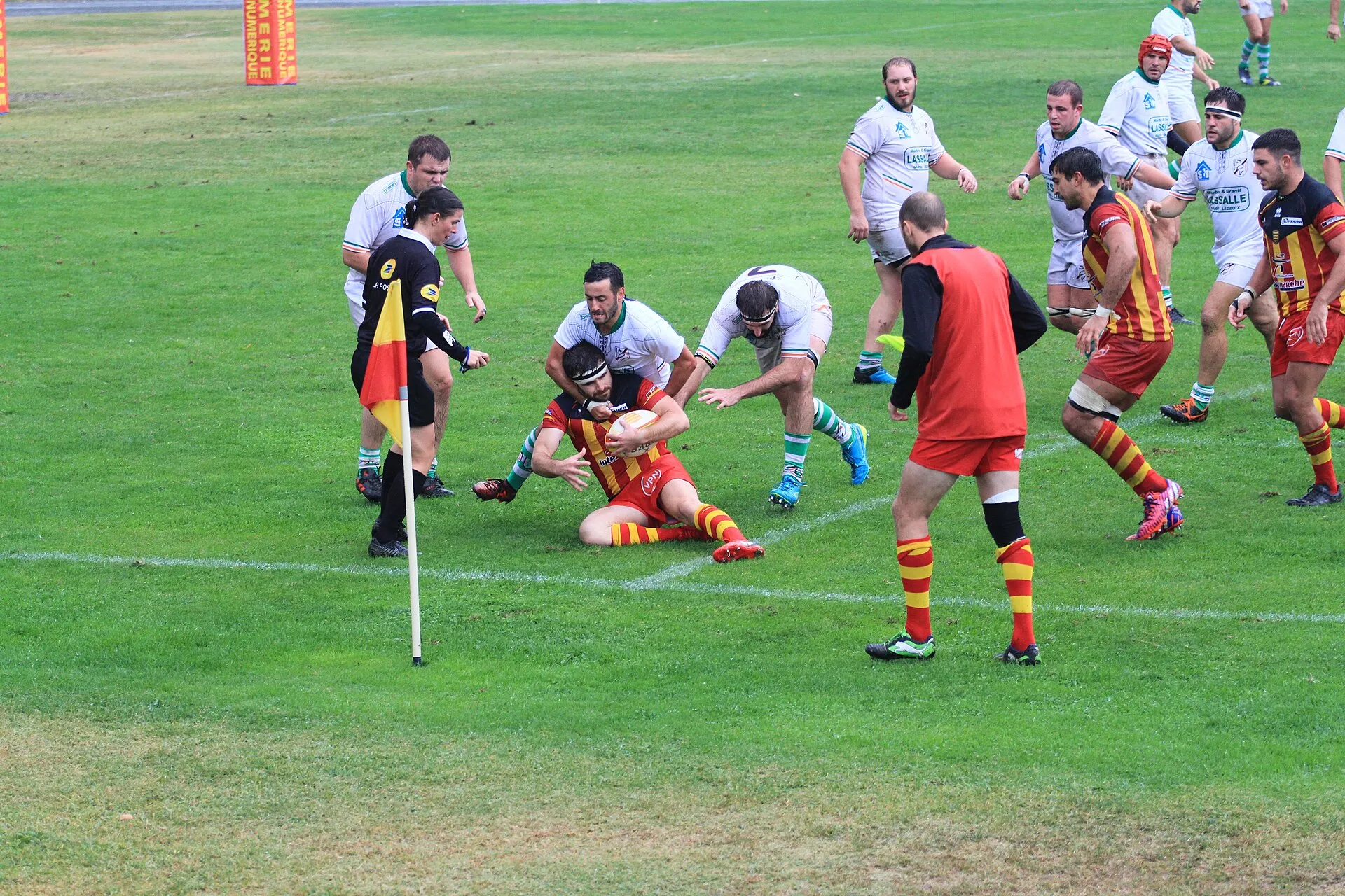 A referee watches closely as a ball carrier goes to ground in a tackle during a rugby match