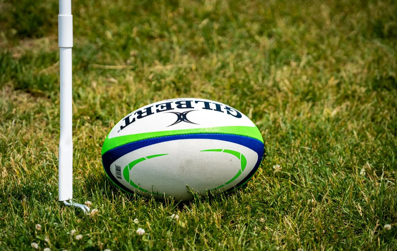 A Gilbert rugby ball resting on the grass beside a goalpost