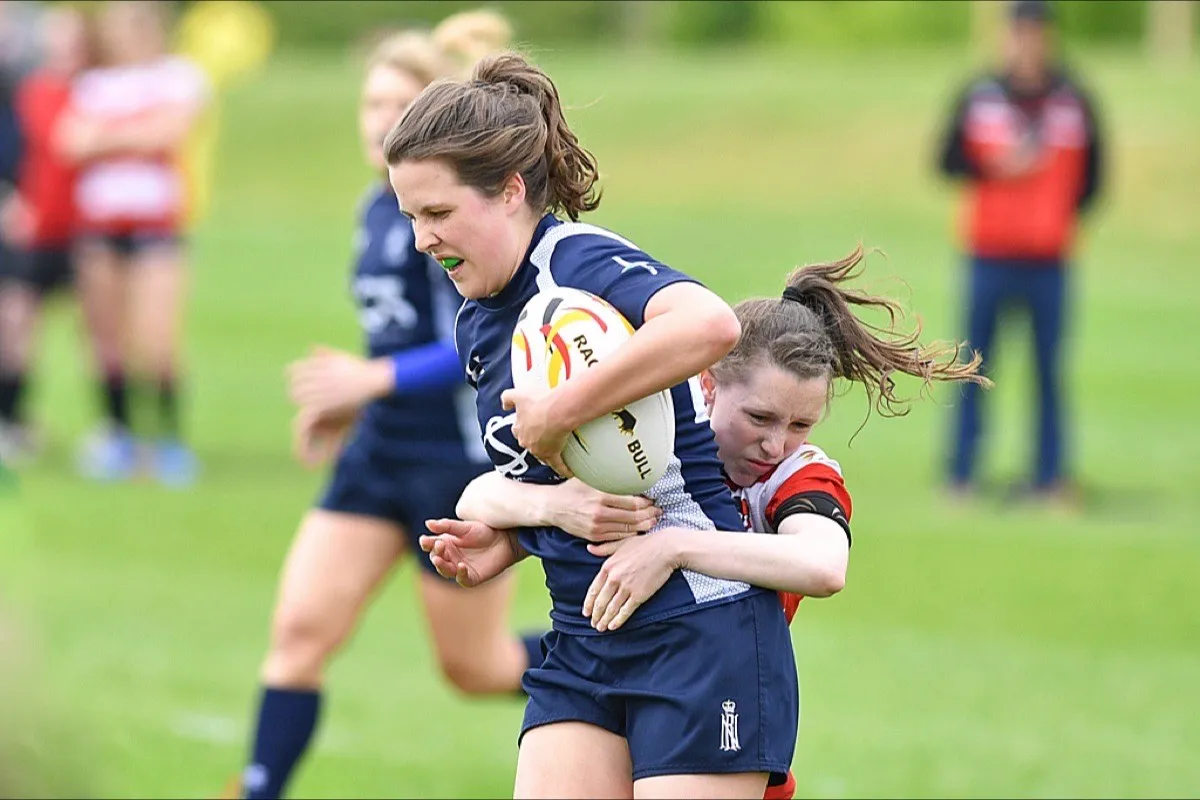 A rugby player is tackled as she carries the ball