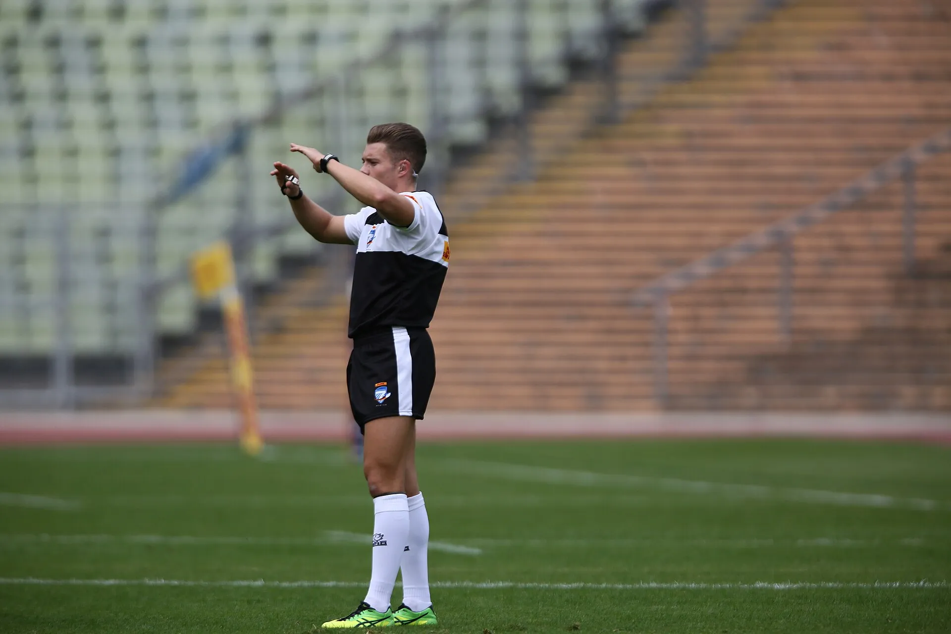 A rugby referee signals a decision in front of an empty stand