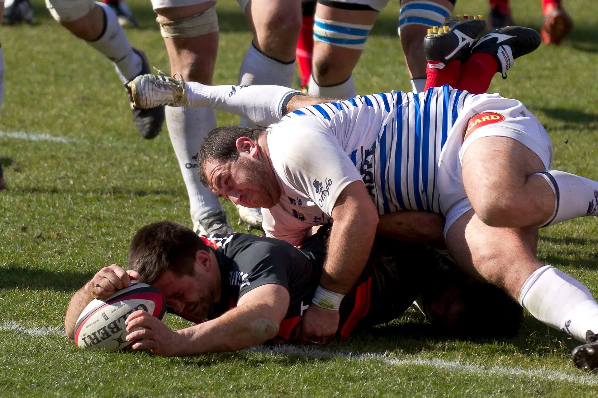 A ball carrier grounds the ball over the try line beneath a tackler