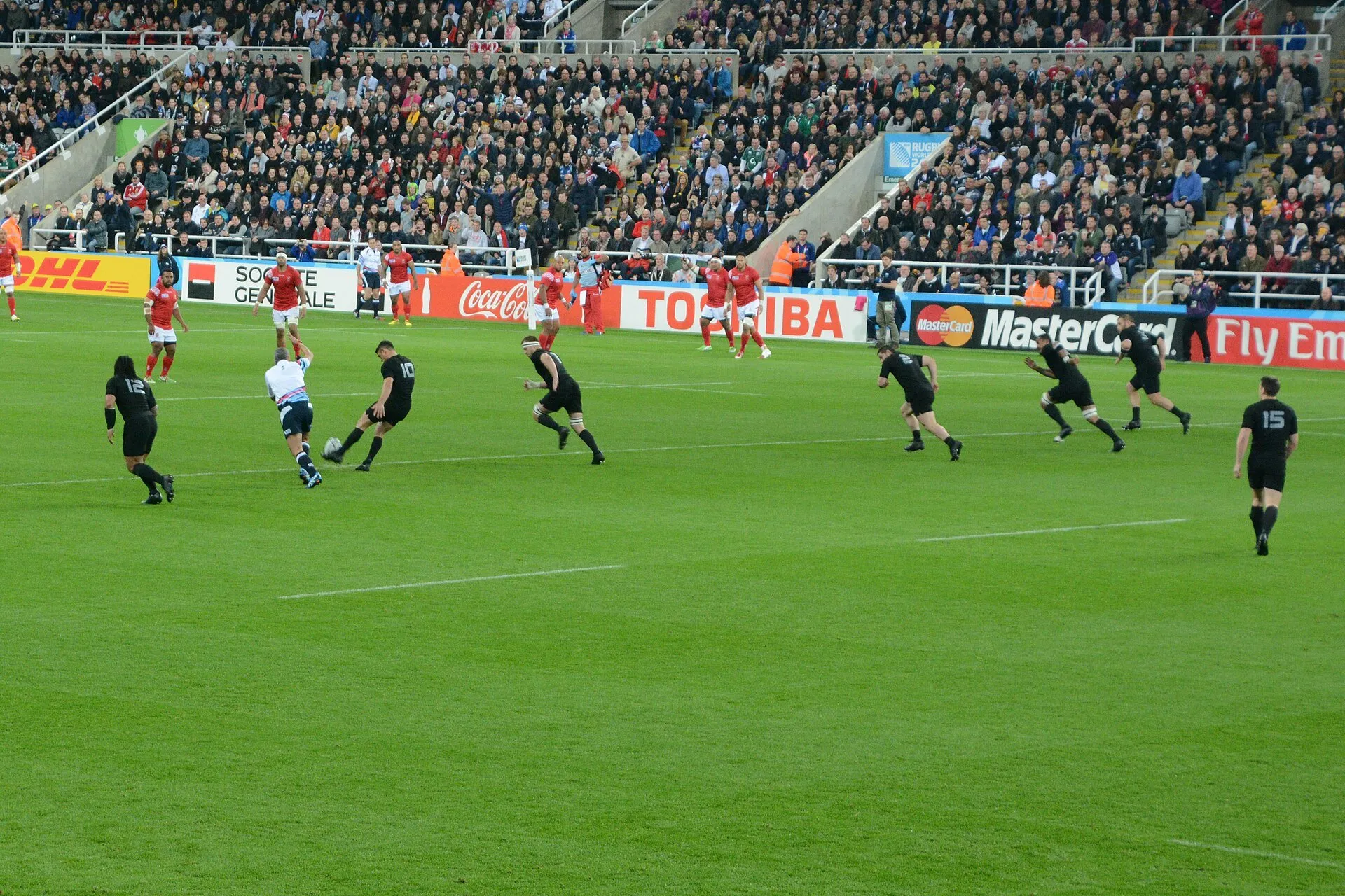 A rugby international kicks off in front of a full stadium lined with sponsor boards