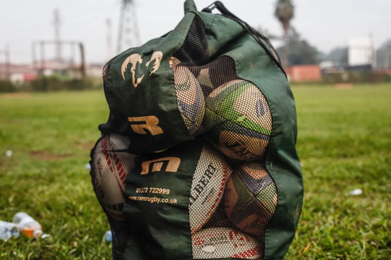 A mesh bag of well-used rugby balls on the side of a grass pitch