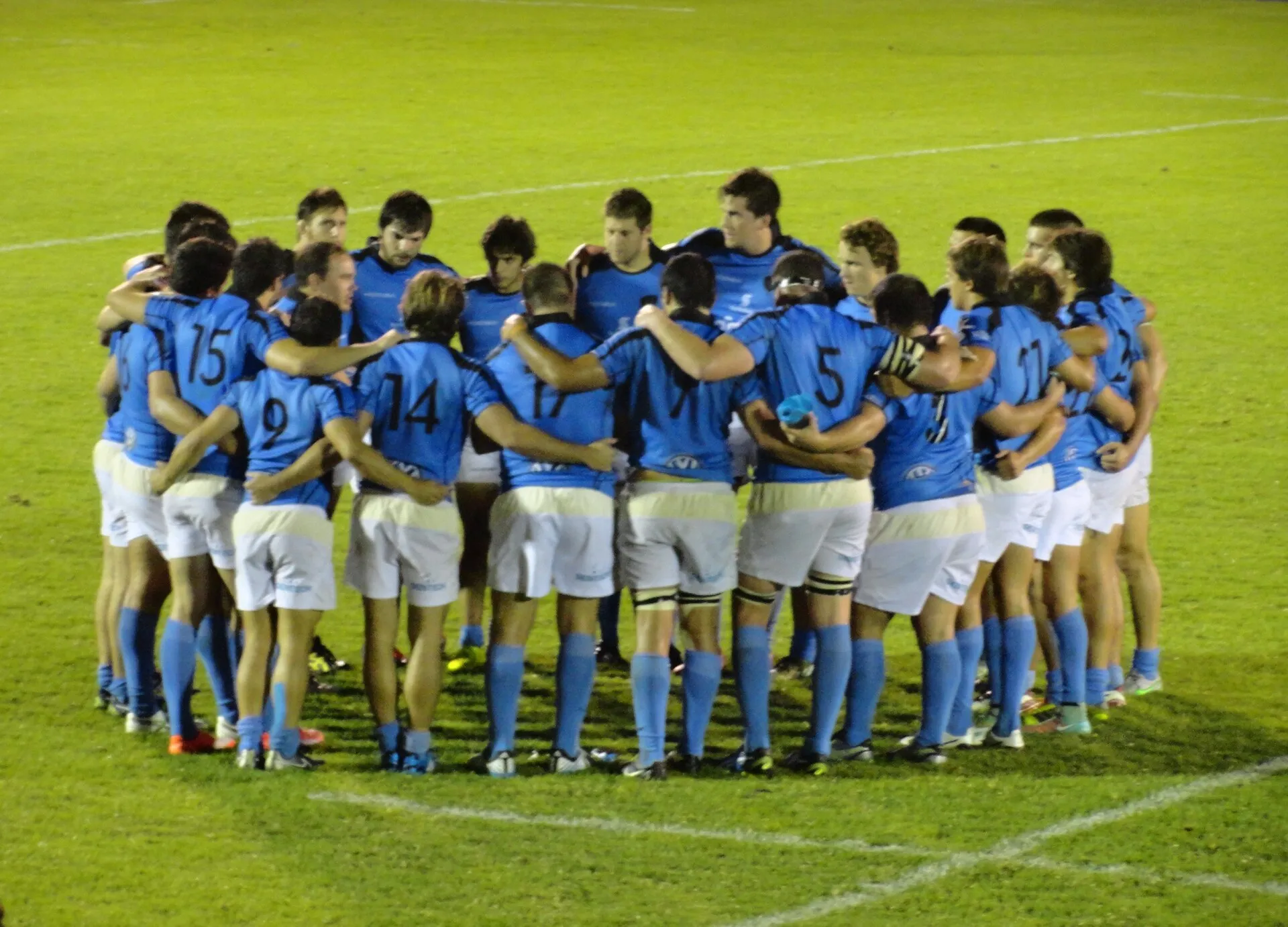 A rugby team gathers in a huddle to listen to their coach