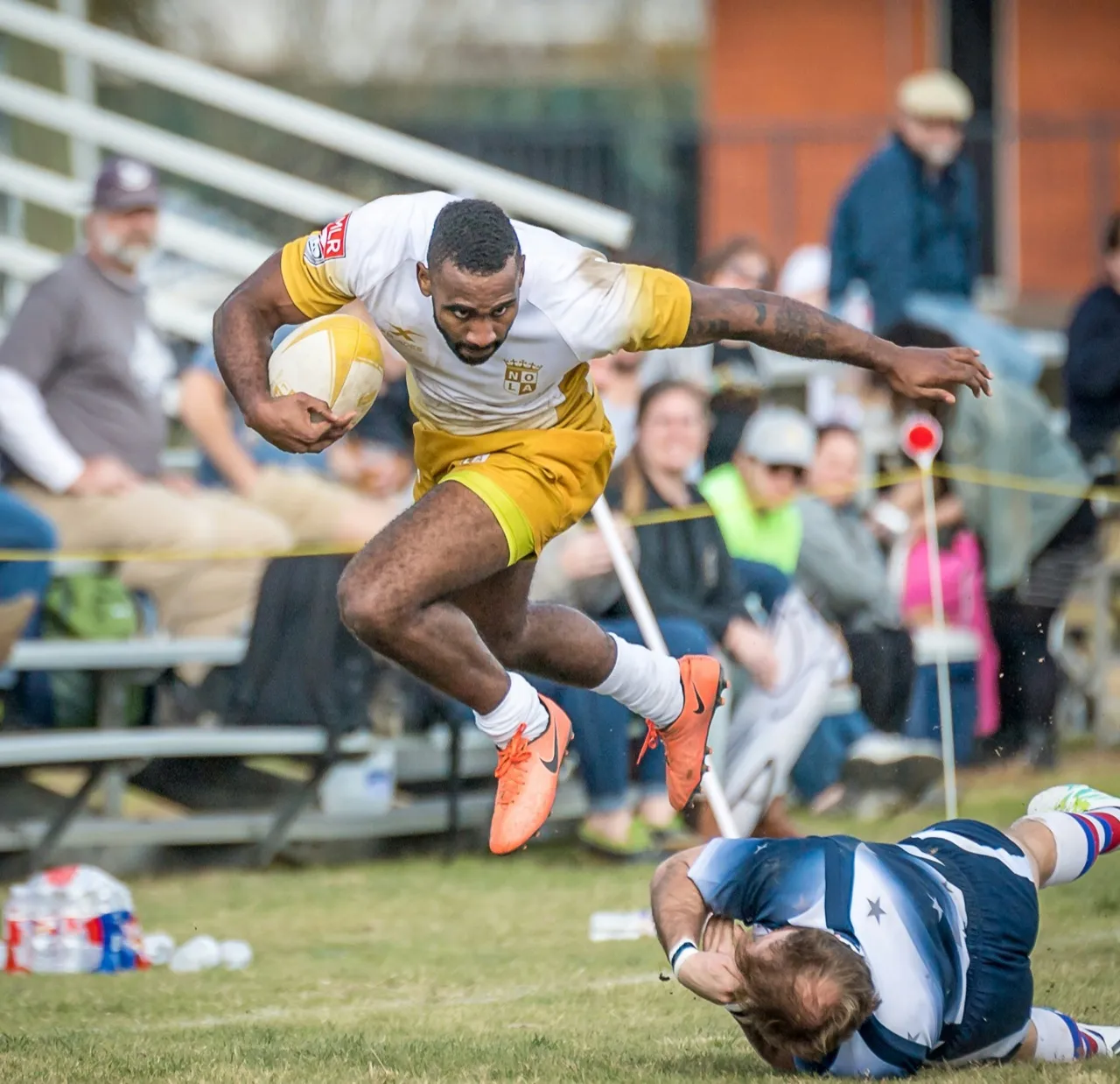 A rugby player in yellow leaps over a falling tackler during a match