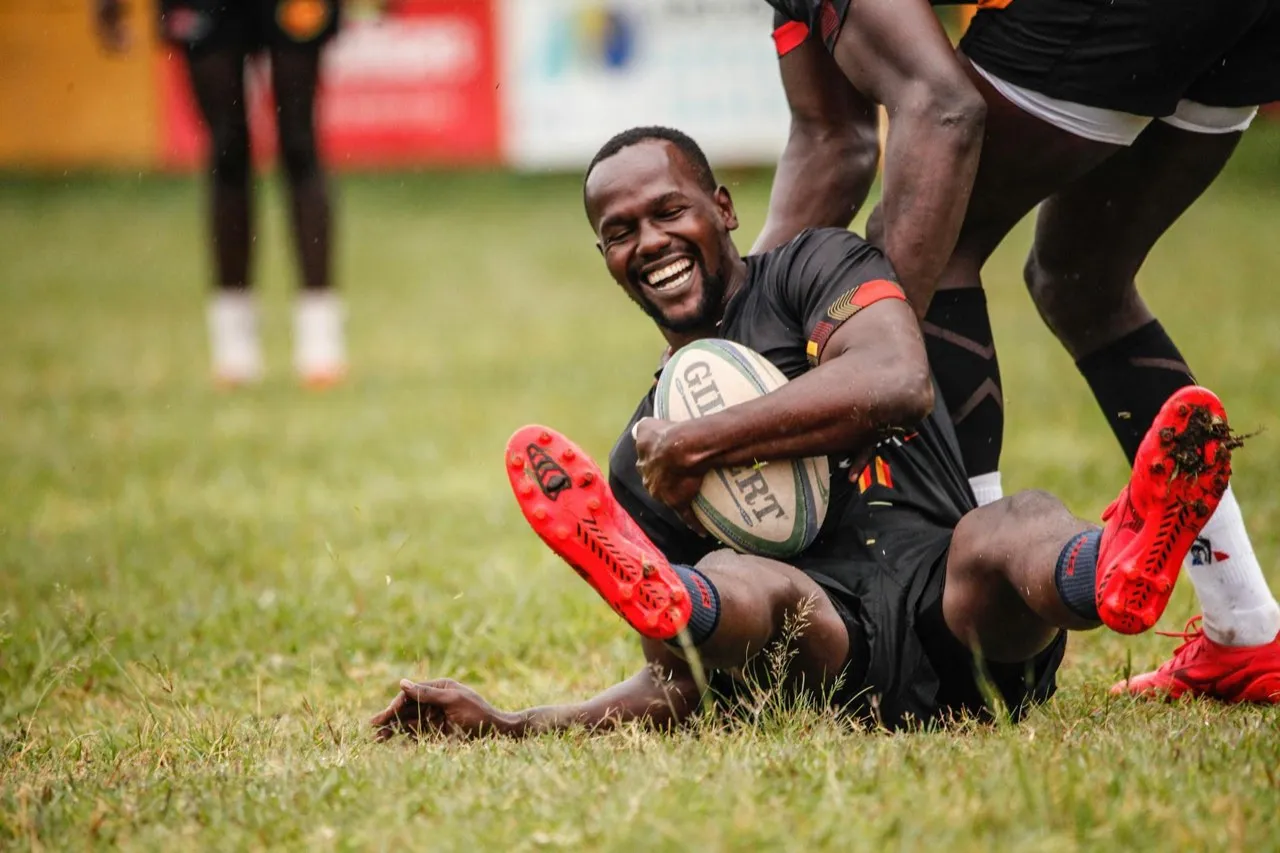 A grinning rugby player sitting on the pitch holding the ball after scoring