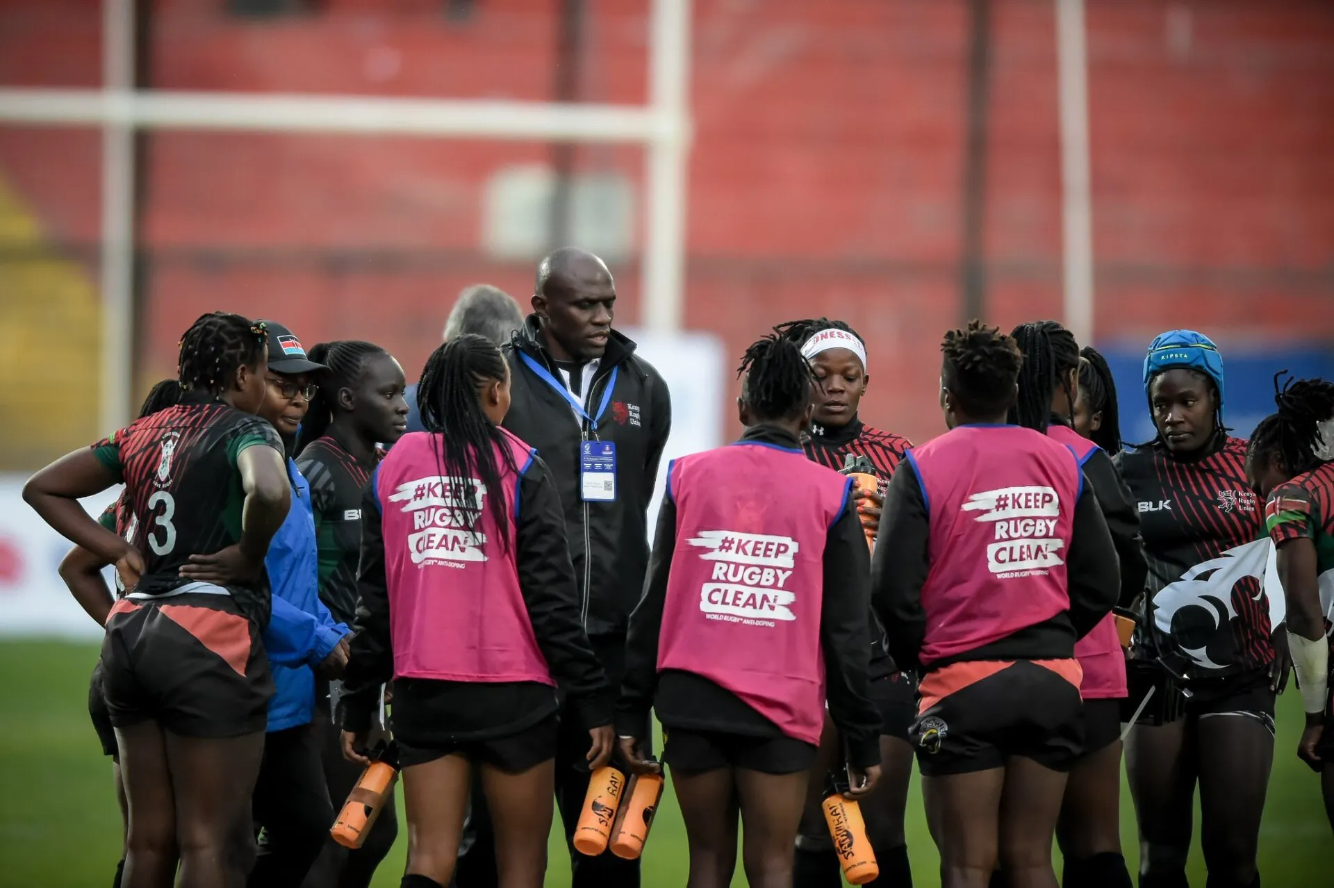A coach talks to a huddle of players in training bibs at half time