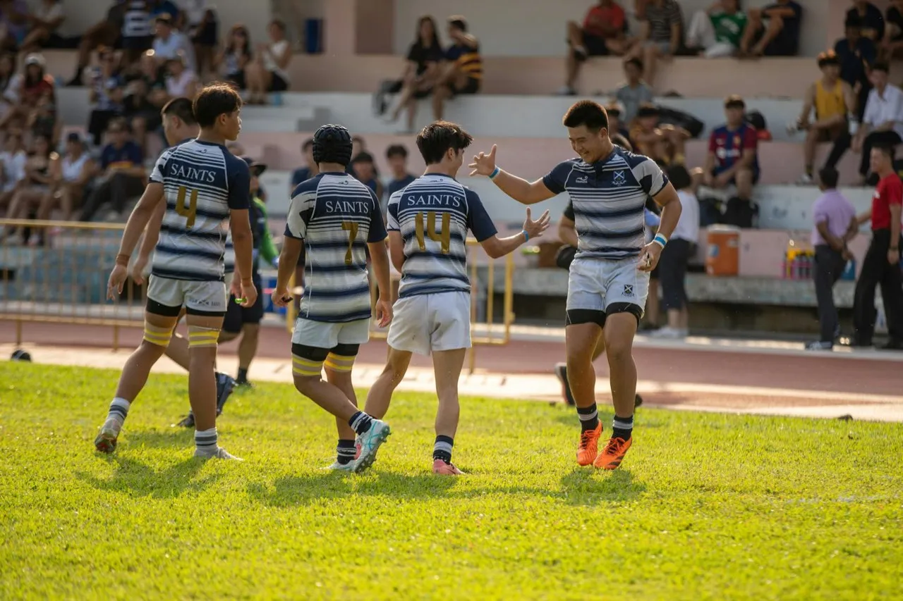 A rugby team in numbered shirts celebrating a score together on the pitch
