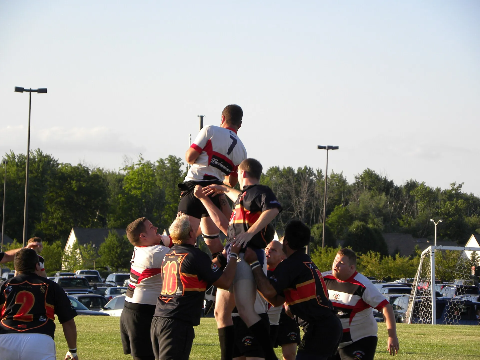 A club rugby lineout with a jumper lifted above the line in evening light