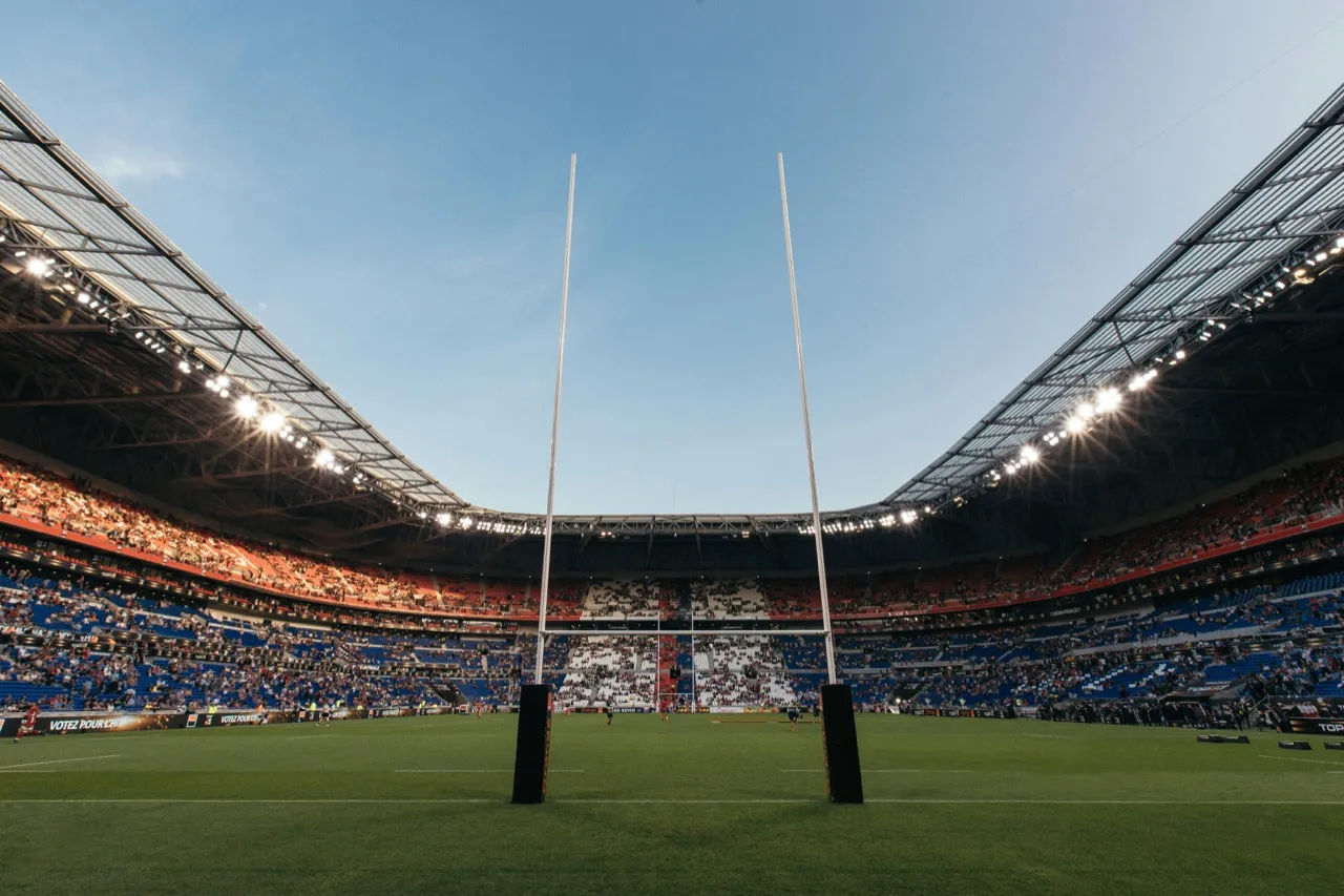 Rugby goalposts in a large floodlit stadium under a blue sky