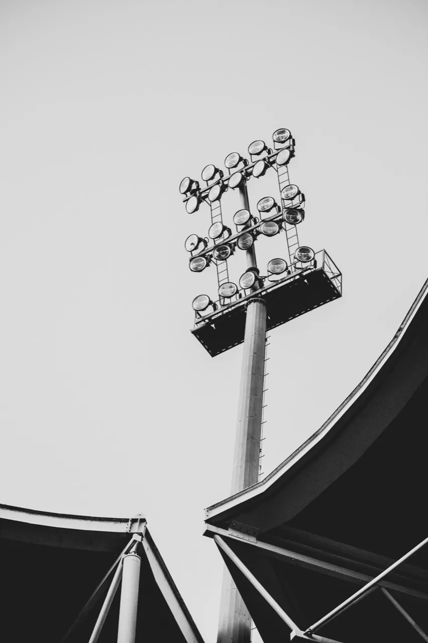 Black-and-white view of stadium floodlights above a stand roof