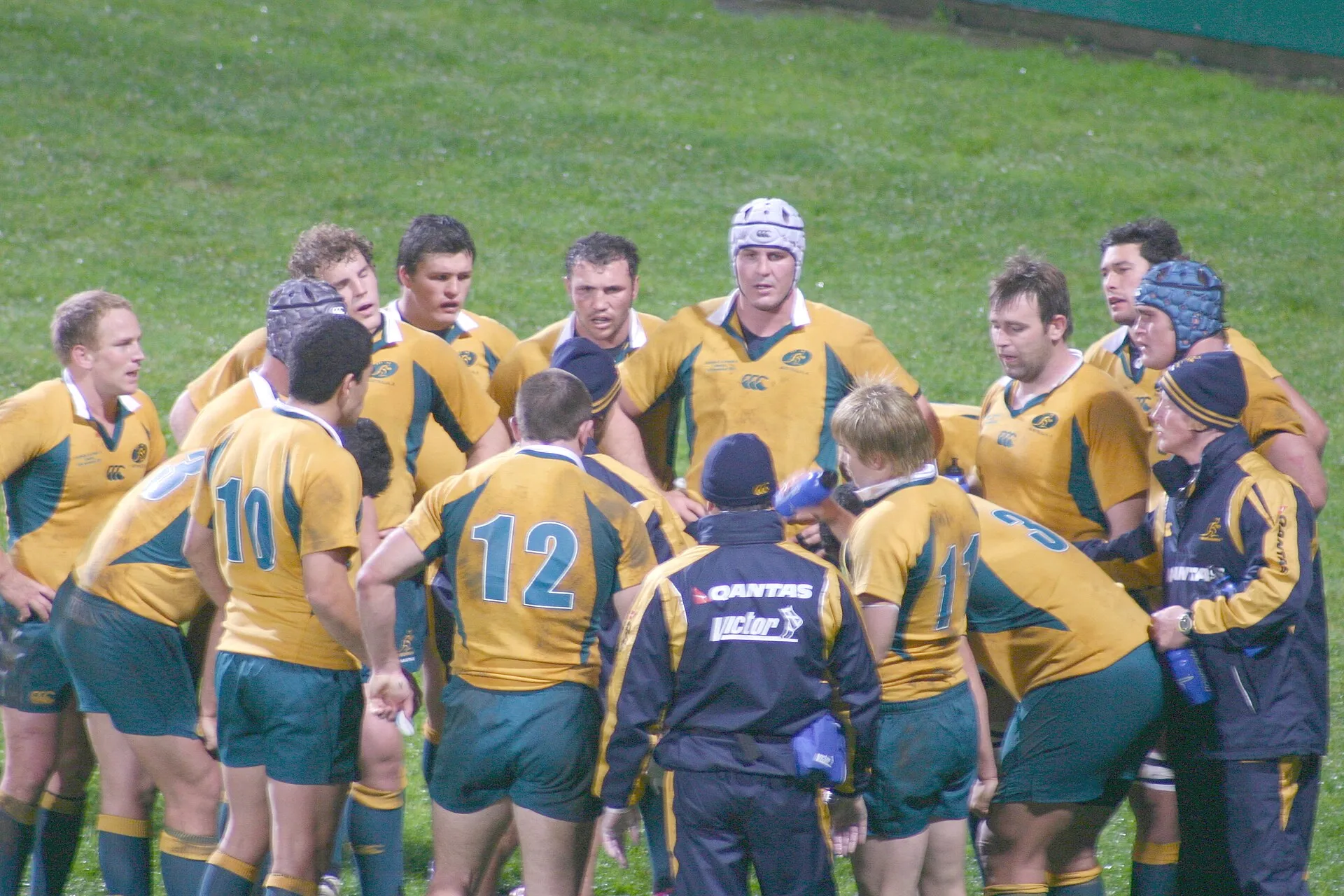 A rugby team gathered in a huddle with coaching staff during a match