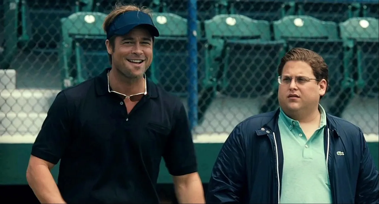 Two baseball executives in conversation beside a ballpark fence