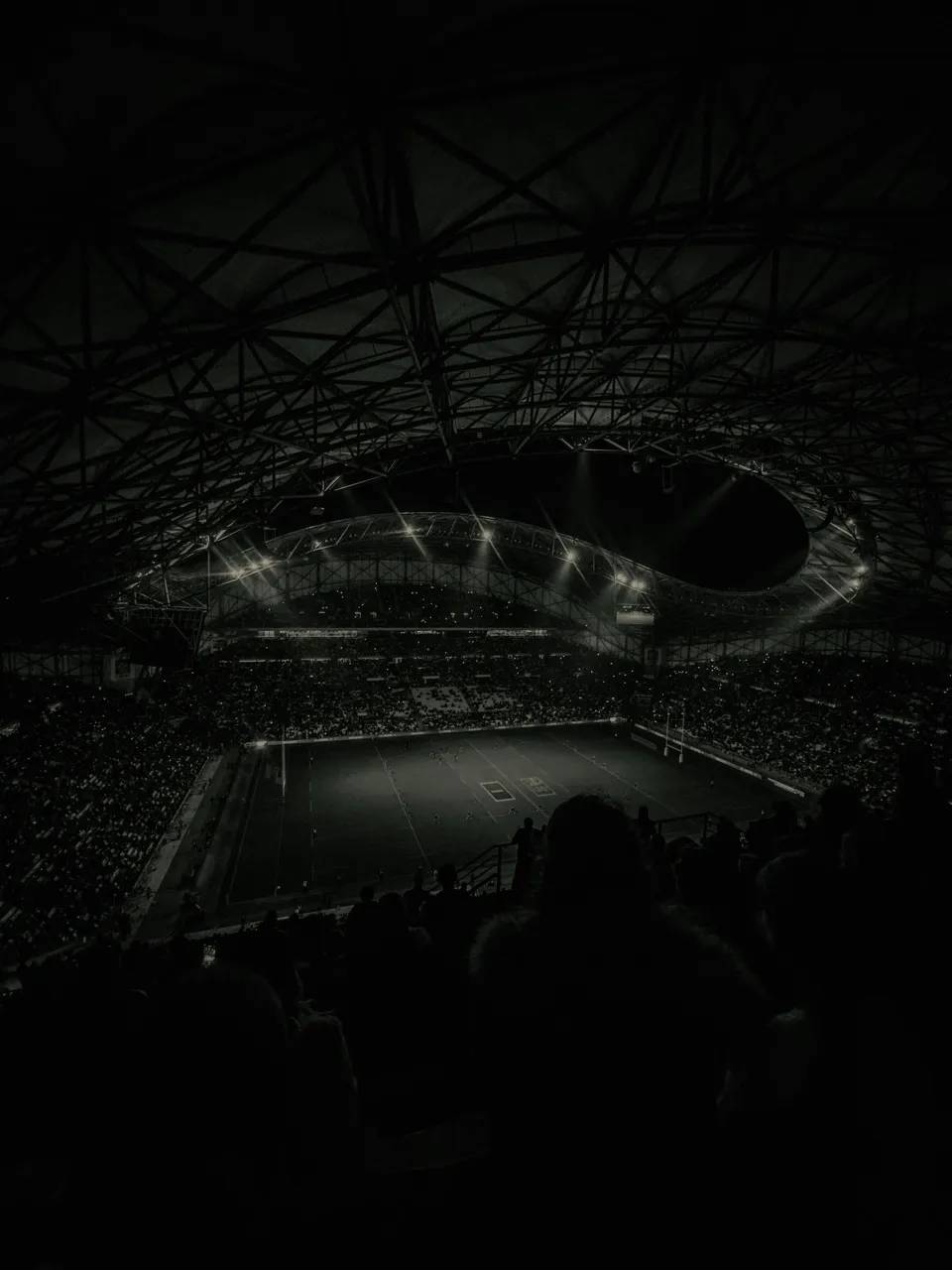 A floodlit pitch inside a darkened domed stadium at night, seen from the stands