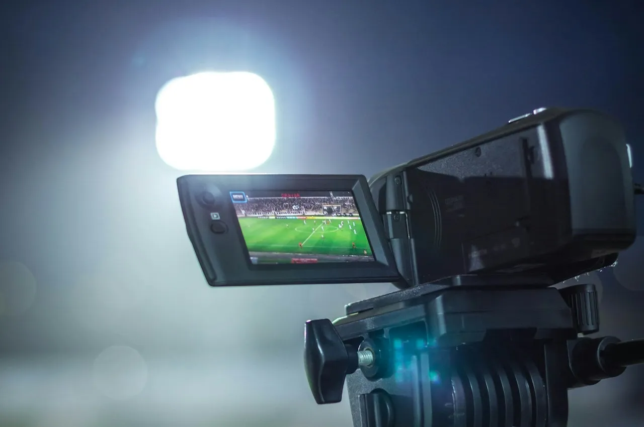 A video camera on a tripod recording a floodlit match