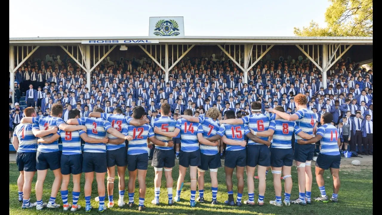 The Nudgee College First XV in a huddle in front of the school crowd at Ross Oval