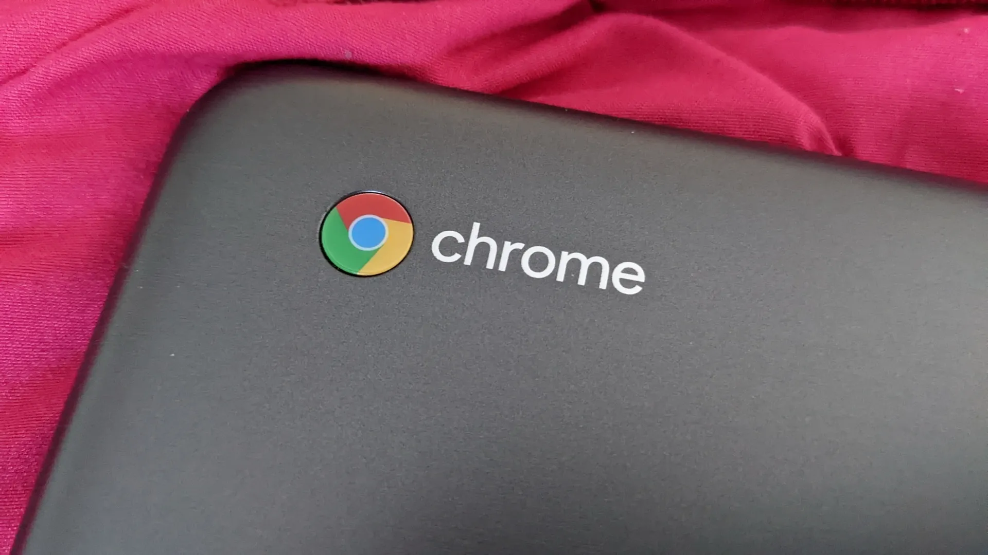 The Chrome logo on the lid of a dark grey Acer Chromebook, lying on a red cloth