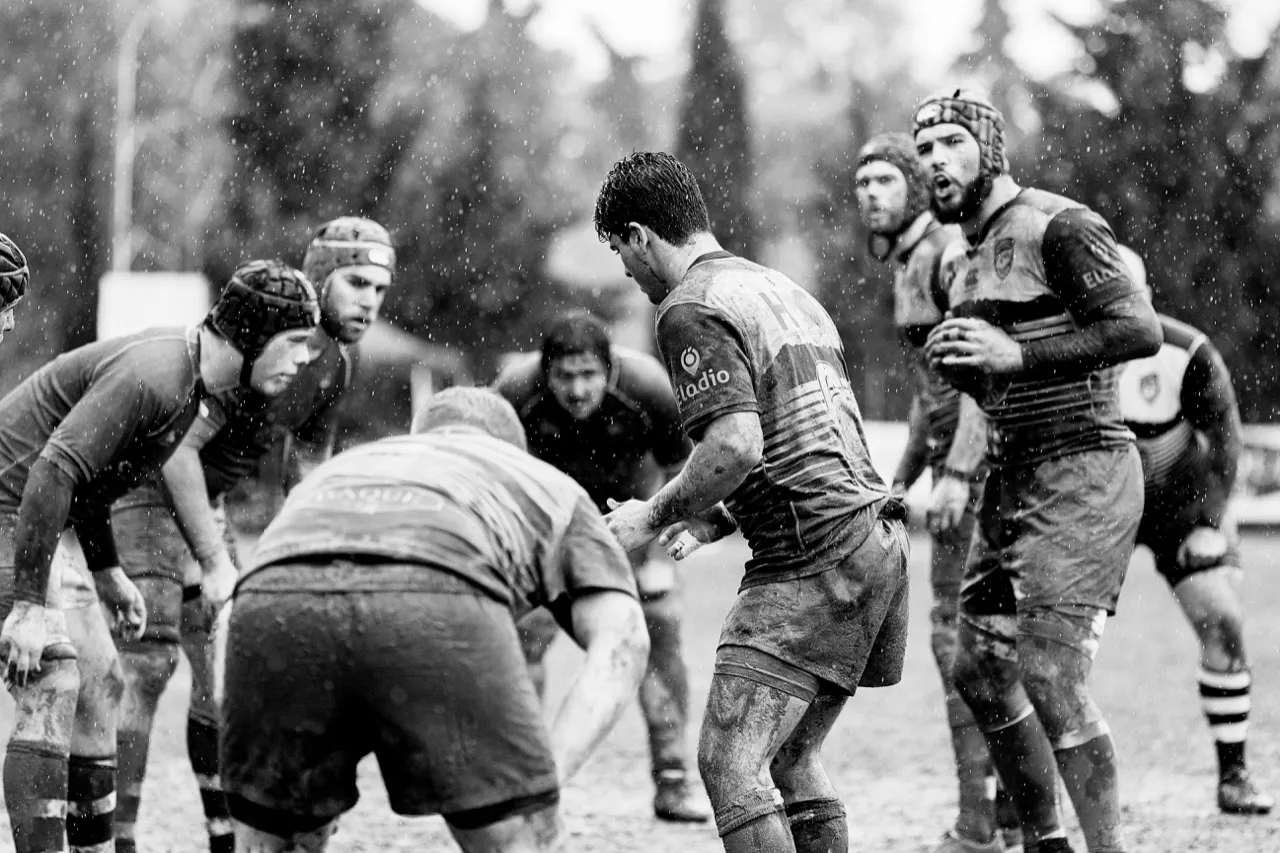 Mud-covered players setting for a scrum in the rain, in black and white