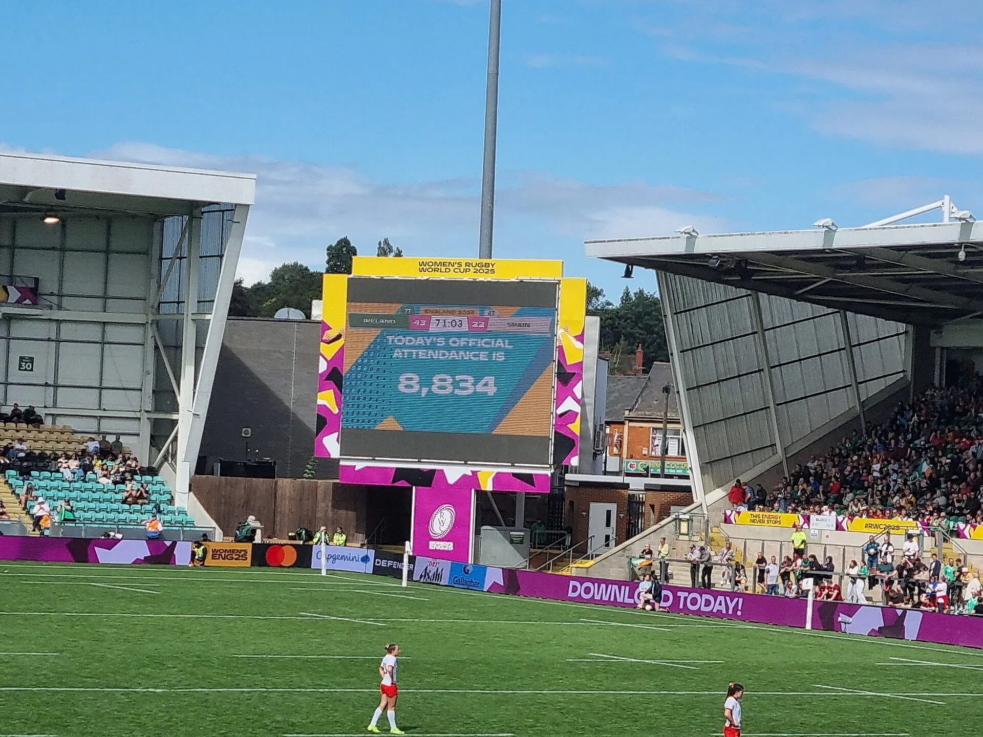 A stadium big screen shows the score, match clock and attendance figures at a rugby ground
