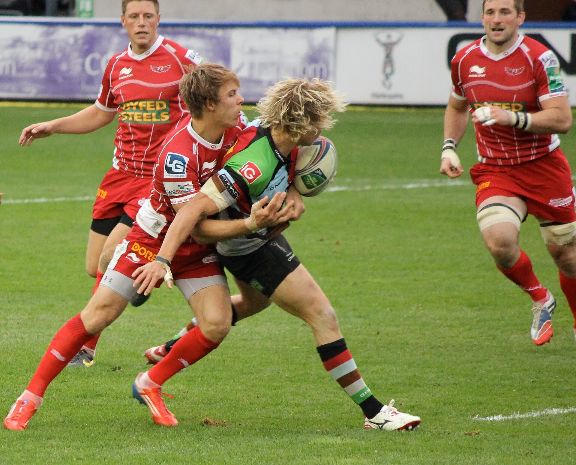 A defender wraps up the ball carrier mid-tackle as support arrives