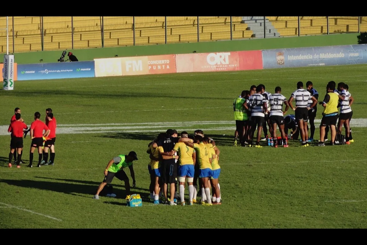 A rugby team gathers in a huddle on the pitch