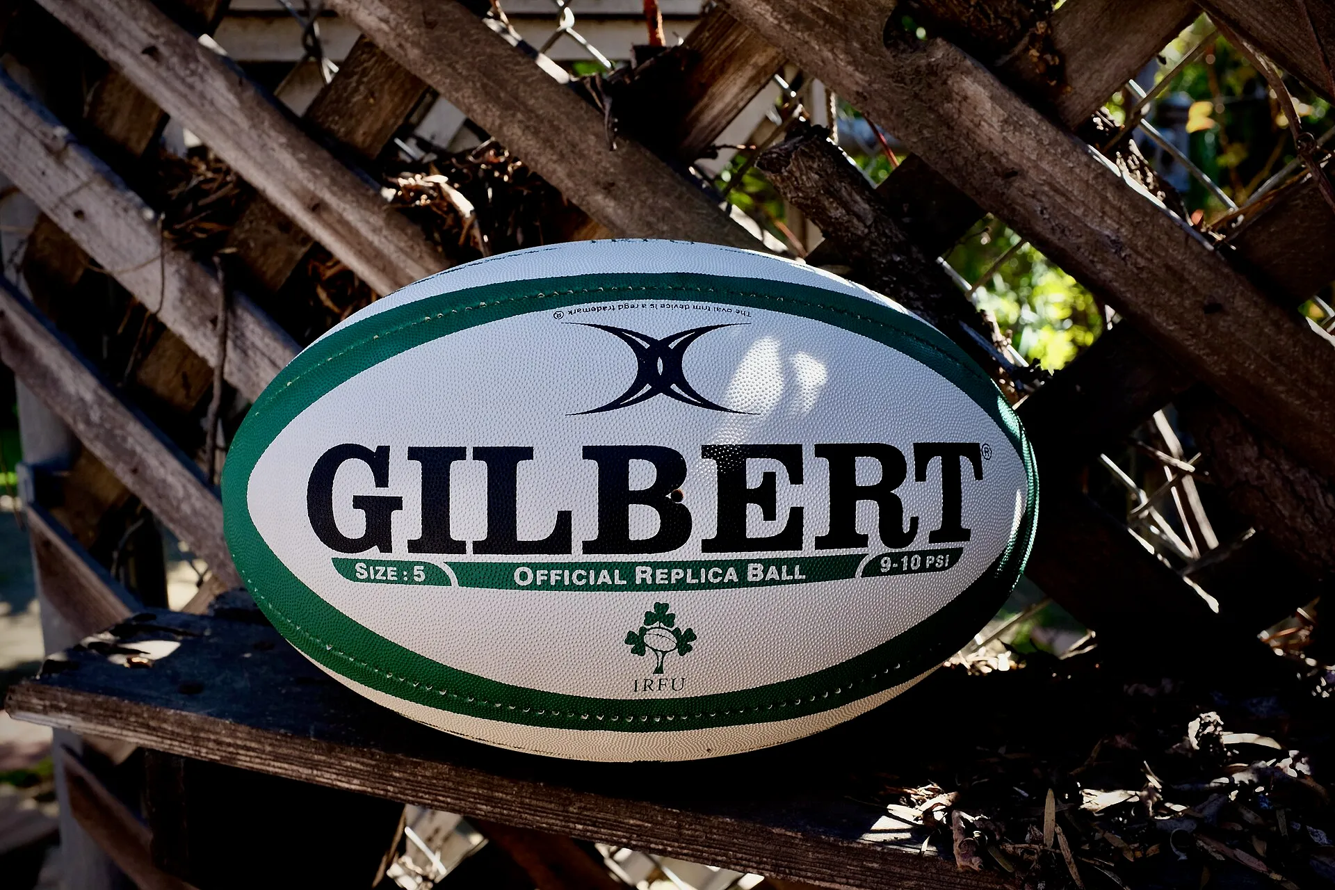 A white Gilbert rugby ball resting on a wooden fence