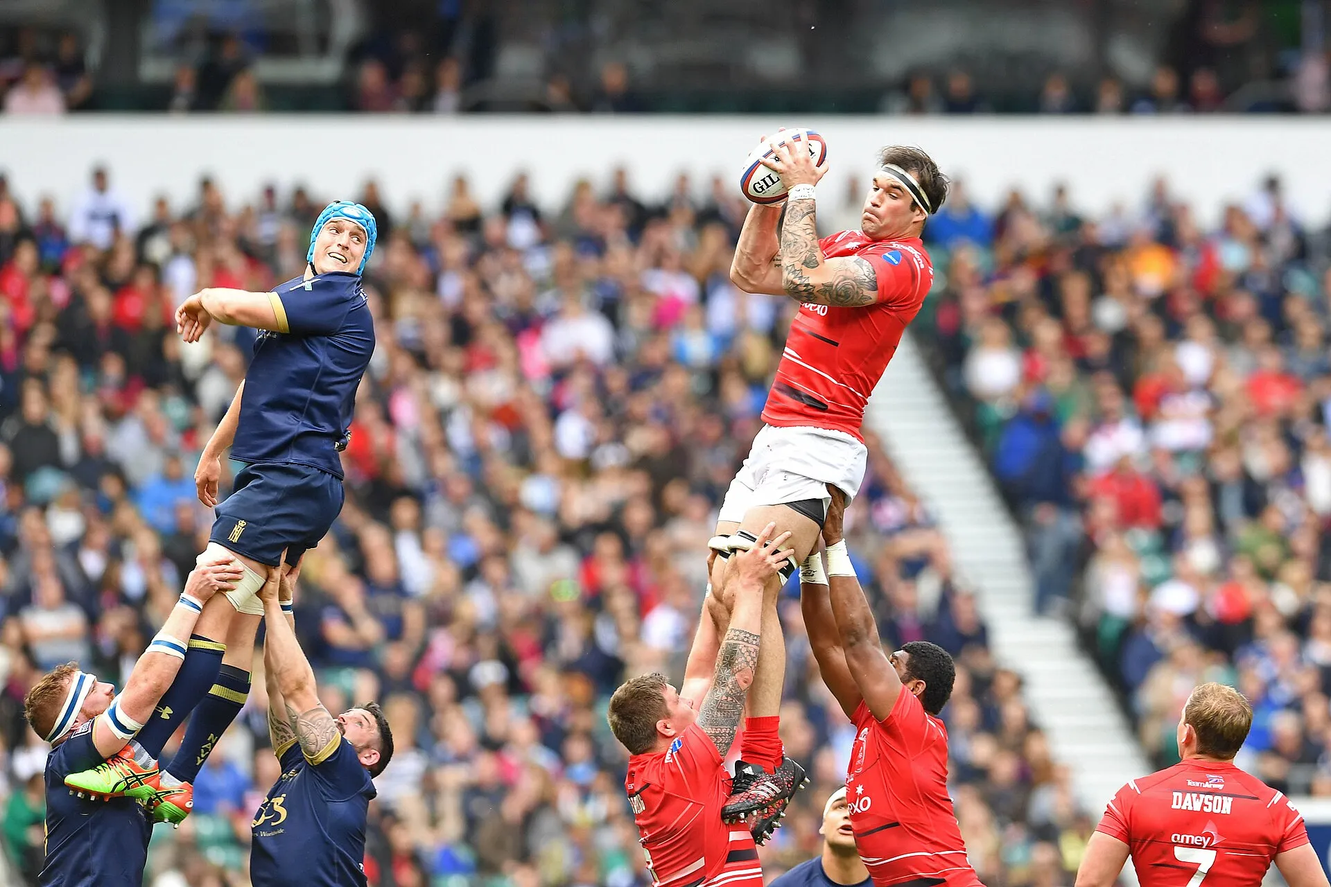 A player claims a high ball in front of a packed rugby stadium crowd