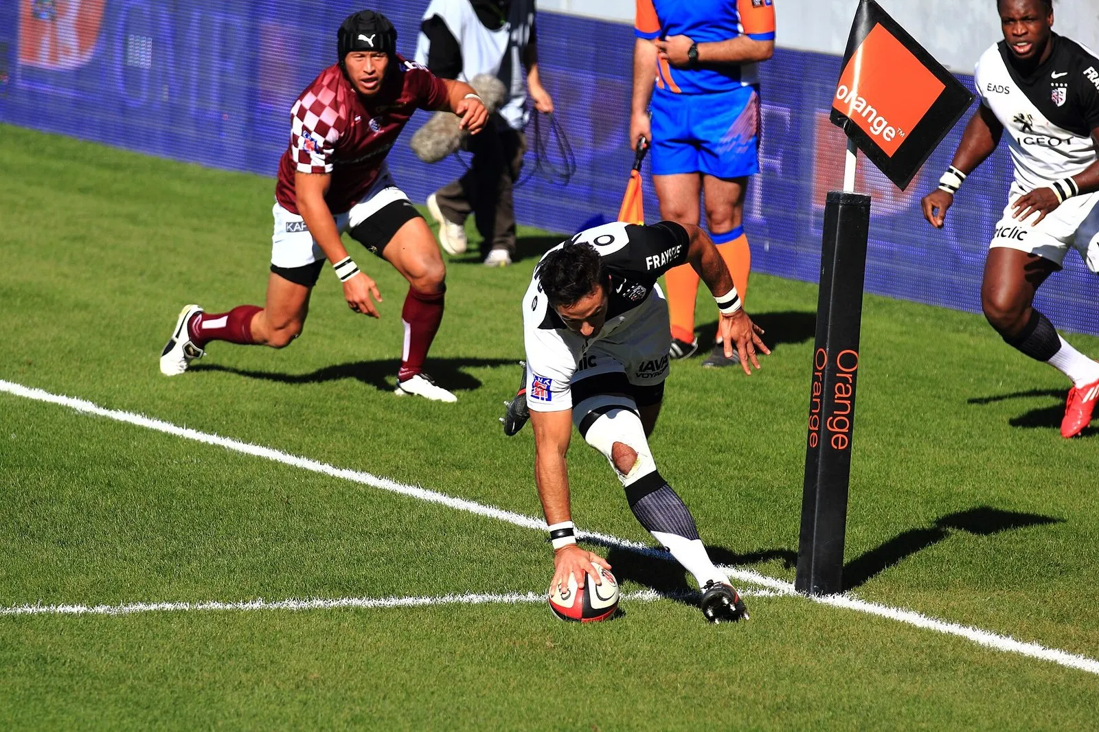 A rugby player dives over the line to score a try beside the posts