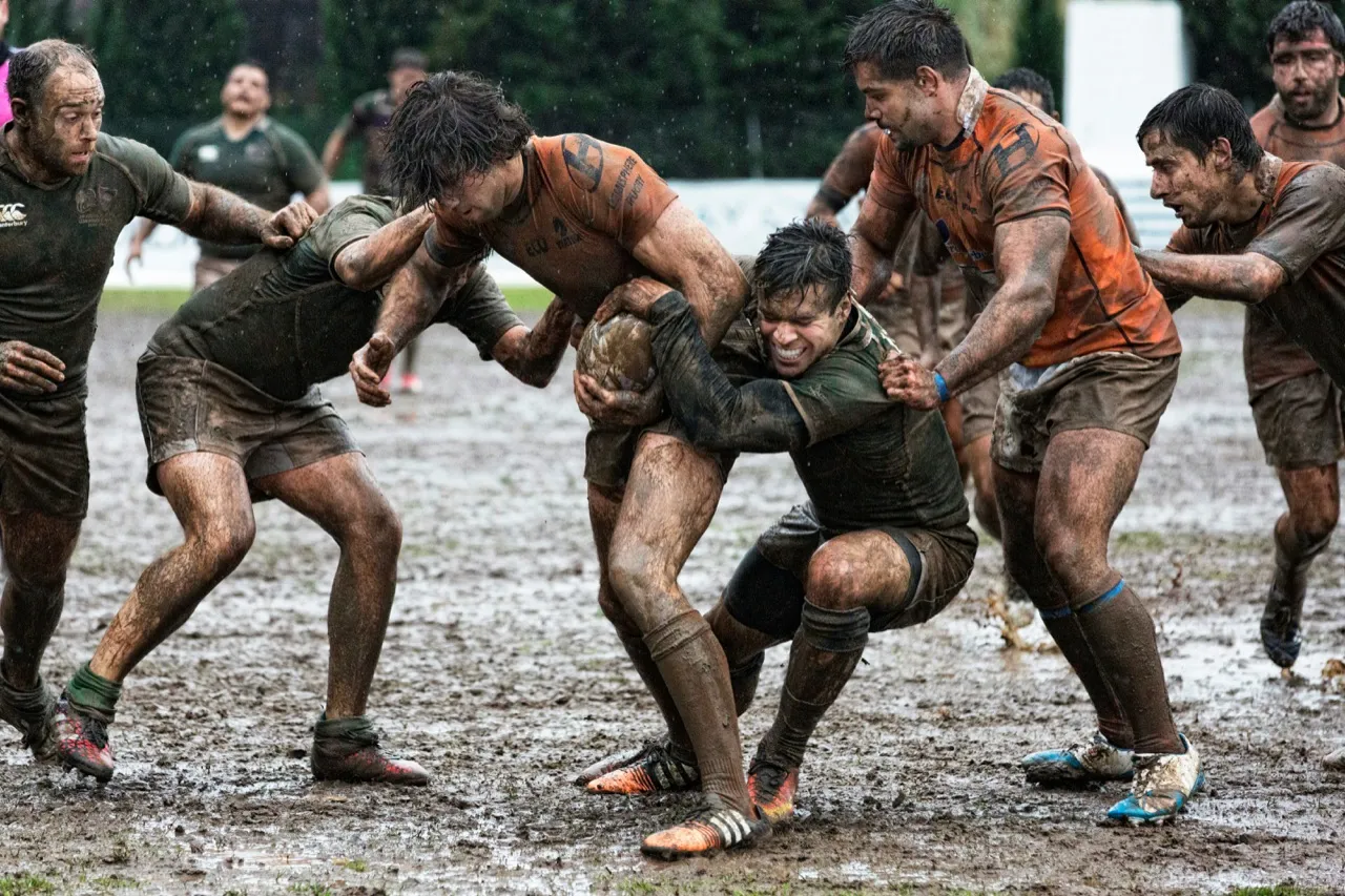Mud-covered players contesting the ball in a maul during a wet match