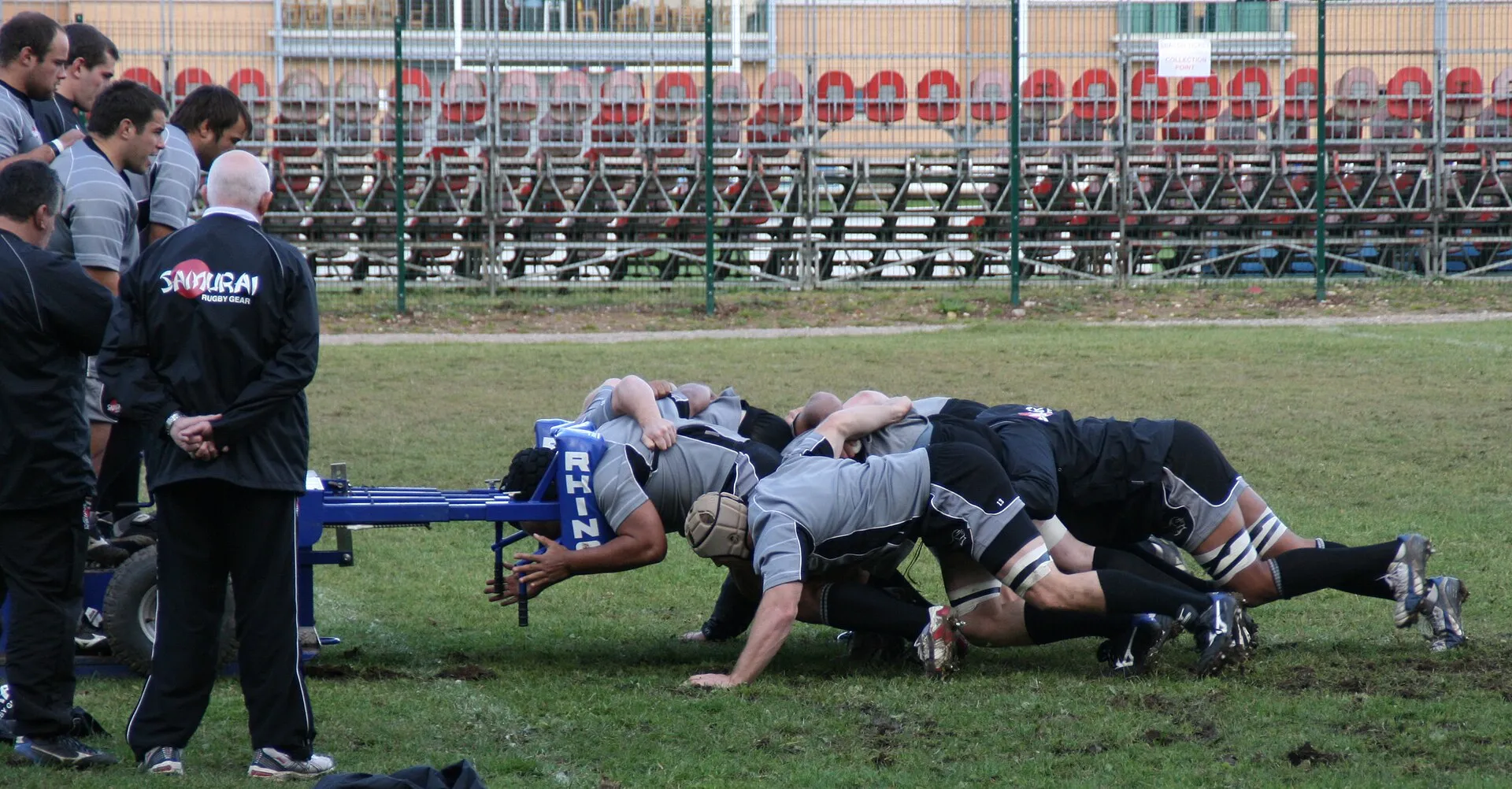 A forward pack driving against a scrum machine while coaches watch